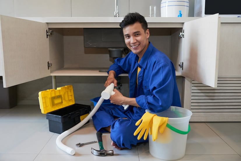 cheerful-asian-plumber-sitting-floor-repairing-kitchen-sink